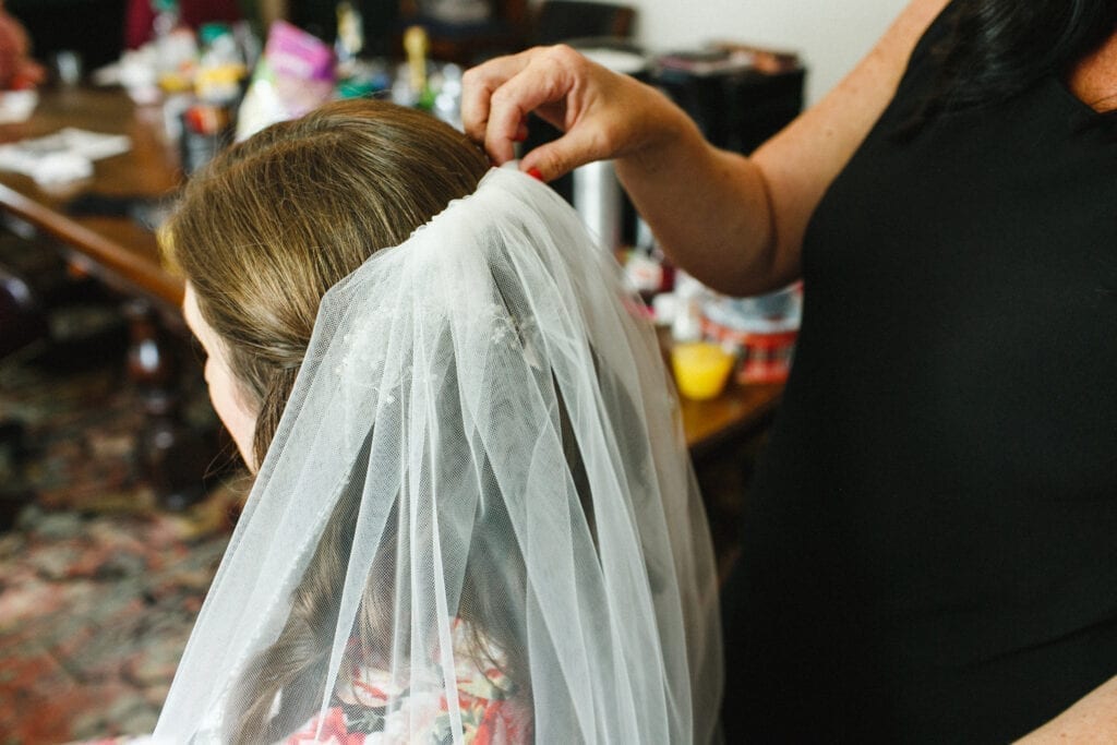 Bella Angel on-location hair and makeup attaching bride's veil
